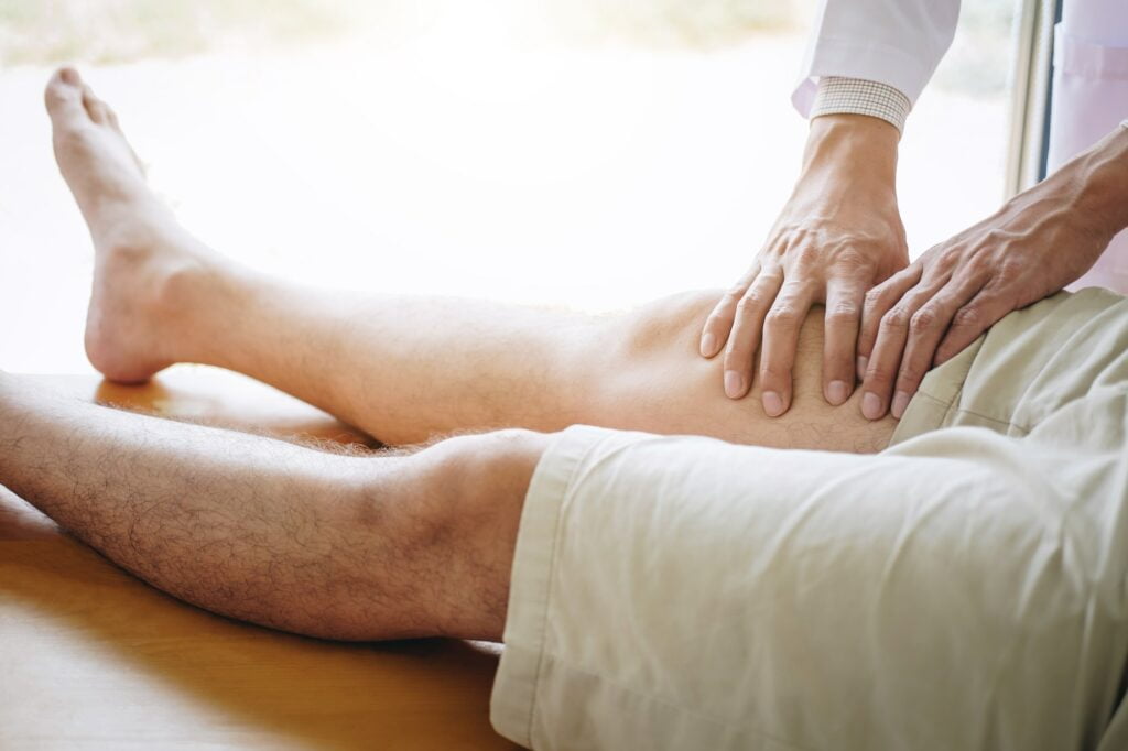 Doctor physiotherapist assisting a male patient while giving exercising treatment massaging the leg