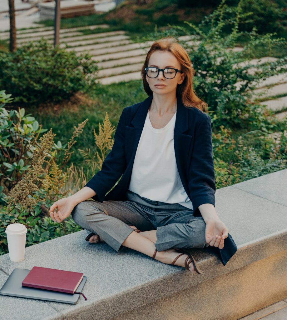 Peaceful calm redhead business woman doing yoga with closed eyes outdoor